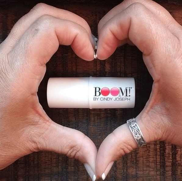 Close up of someone making a heart with their hands. In the middle is a lipstick that says BOOM! By Cindy Joseph