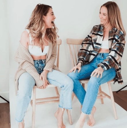 Founders of LAC Swim. Alex Bennett is sitting on the left and Paige Harris is sitting on the right. They are both wearing white LAC swim tops and light. blue jeans